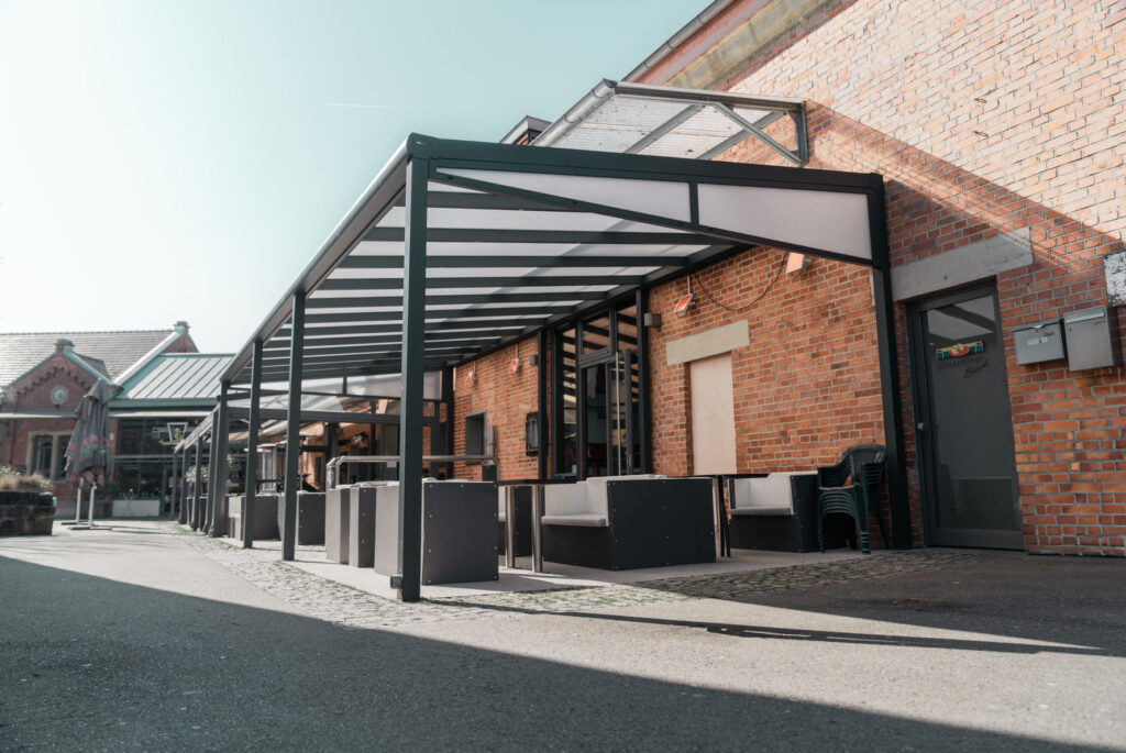 &Uuml;berdachte Terrasse mit Sitzgelegenheiten vor einem Backsteingeb&auml;ude bei sonnigem Wetter