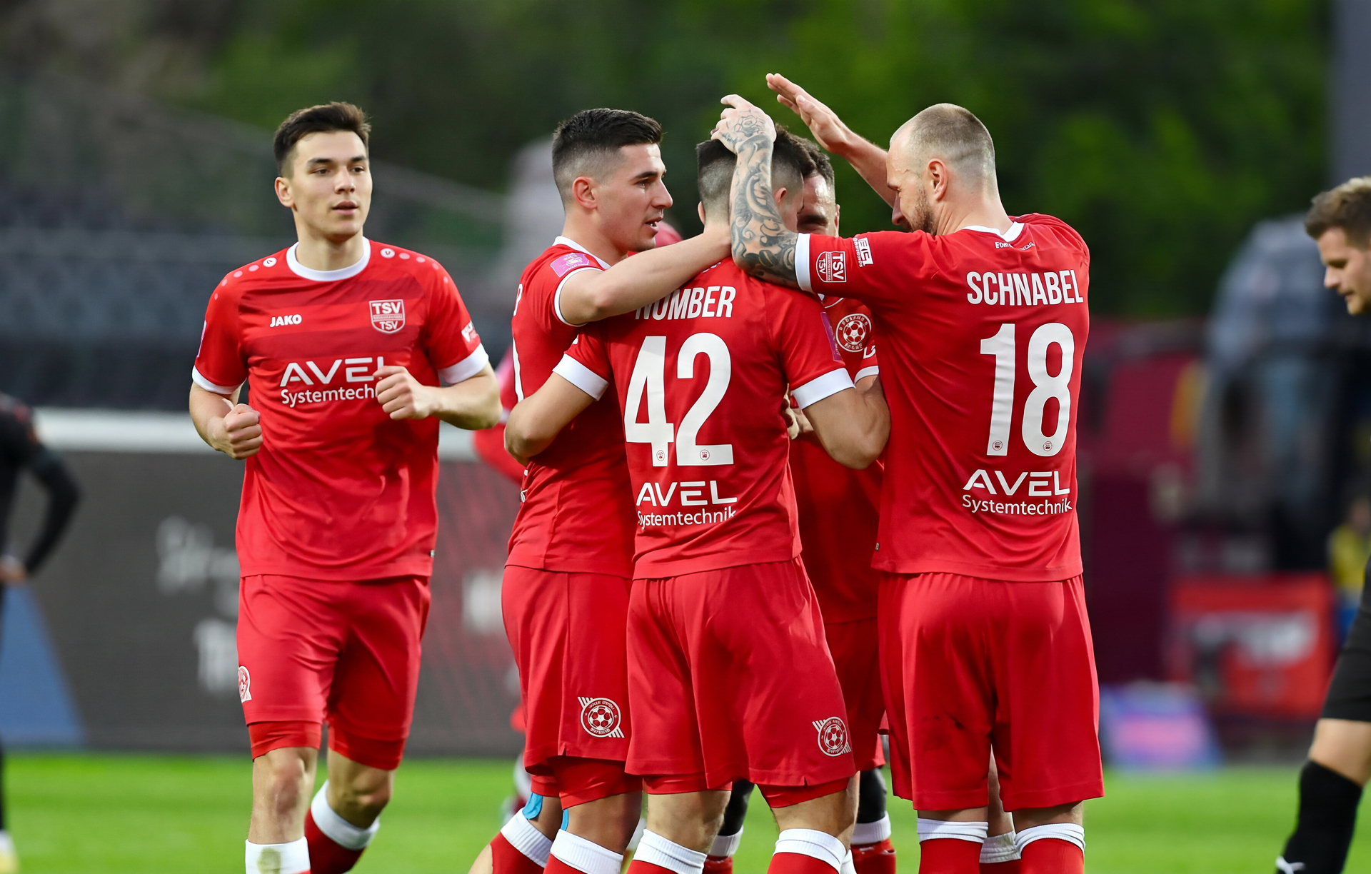 Fußballspieler in roten Trikots umarmen sich auf dem Spielfeld.