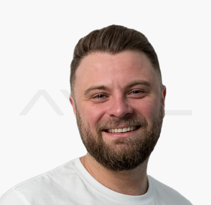 Lächelnde Person mit Bart und weißem T-Shirt vor weißem Hintergrund.
