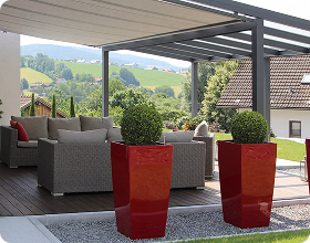 Moderne Terrasse mit Pergola, Sitzecke und roten Pflanzkübeln in bergiger Landschaft.