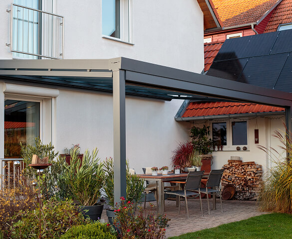 Moderne Terrasse mit Überdachung, Tisch, Stühlen und Pflanzen.