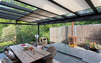 Moderne Terrasse mit Glasdach, Holztisch und Gartenblick.