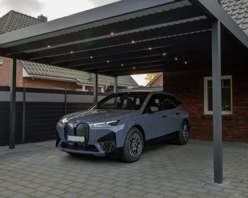 Modernes Auto unter beleuchtetem Carport auf gepflastertem Boden.