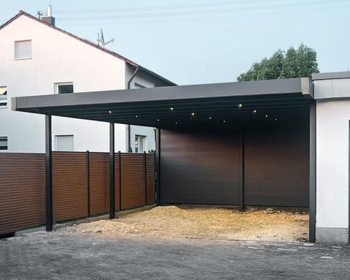 Moderner Carport neben einem weißen Wohnhaus mit angrenzendem Holzzaun.