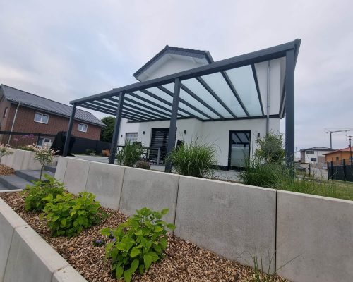 Modernes Haus mit überdachter Terrasse und angelegtem Garten.