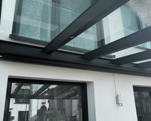 Glasüberdachung mit Metallträgern an Hausfassade, moderne Architekturmerkmale.