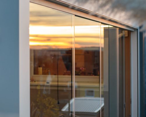 Glasfenster reflektiert Sonnenuntergang in modernem Gebäude mit sichtbarer Innen- und Außenseite.