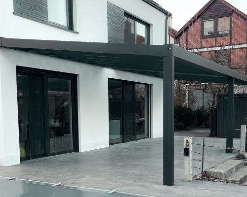 Moderne Terrasse mit Überdachung an einem zweistöckigen weißen Haus.