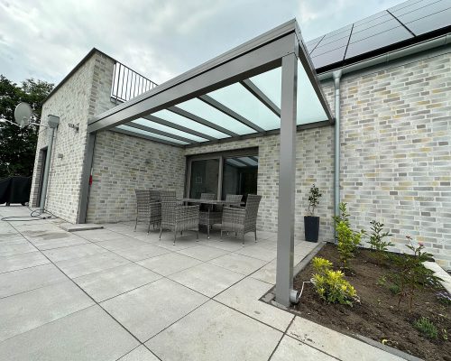 Überdachte Terrasse mit Gartenmöbeln neben einem modernen Ziegelhaus.