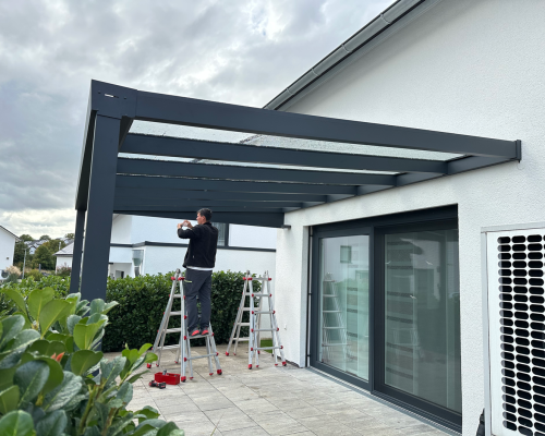 Aufbau einer Terrassenüberdachung vor einem modernen Haus mit Leiter