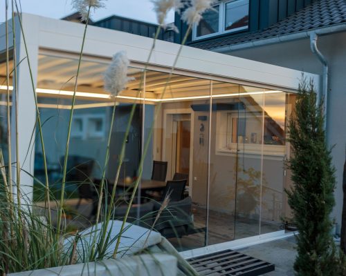 Moderner Wintergarten mit Glaswänden neben einem Wohnhaus.